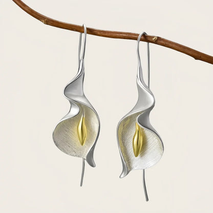 Silver and gold leaf-shaped earrings hanging from a branch on a light background