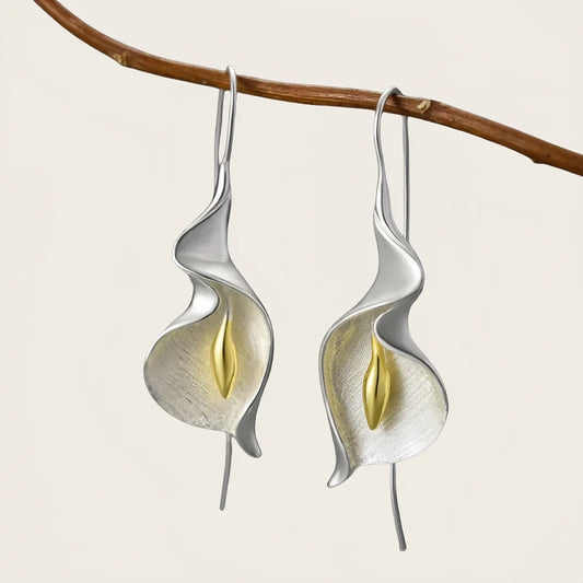 Silver and gold leaf-shaped earrings hanging from a branch on a light background
