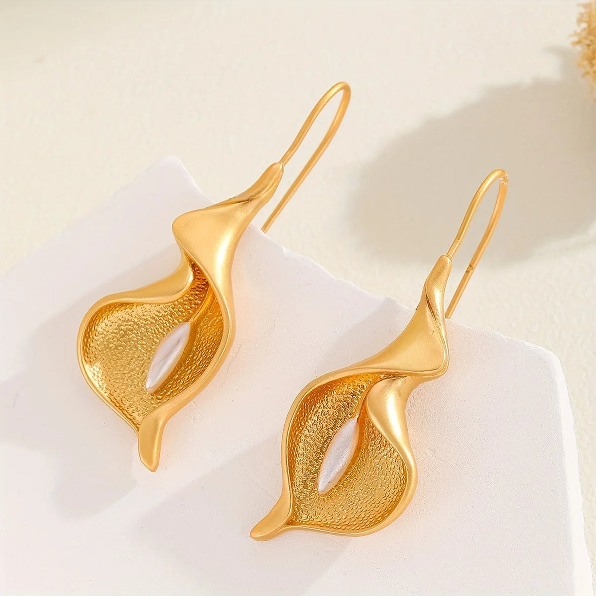 Gold leaf-shaped earrings on a light background