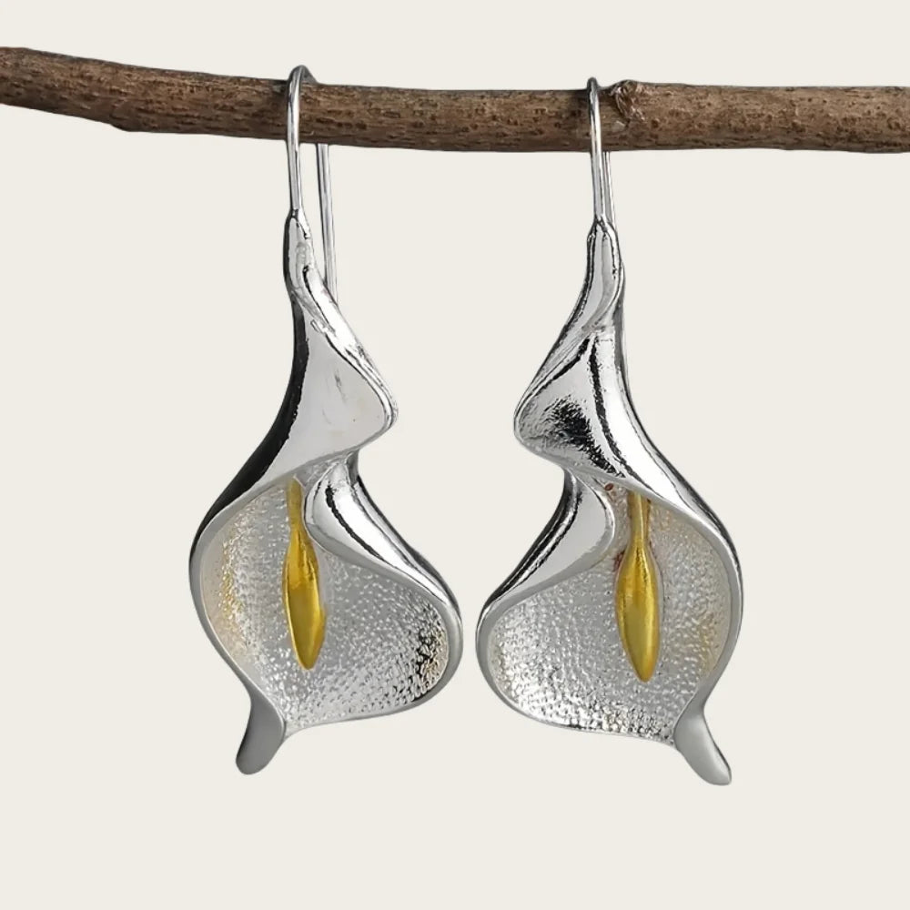 Silver calla lily earrings with gold centers on a branch against a white background